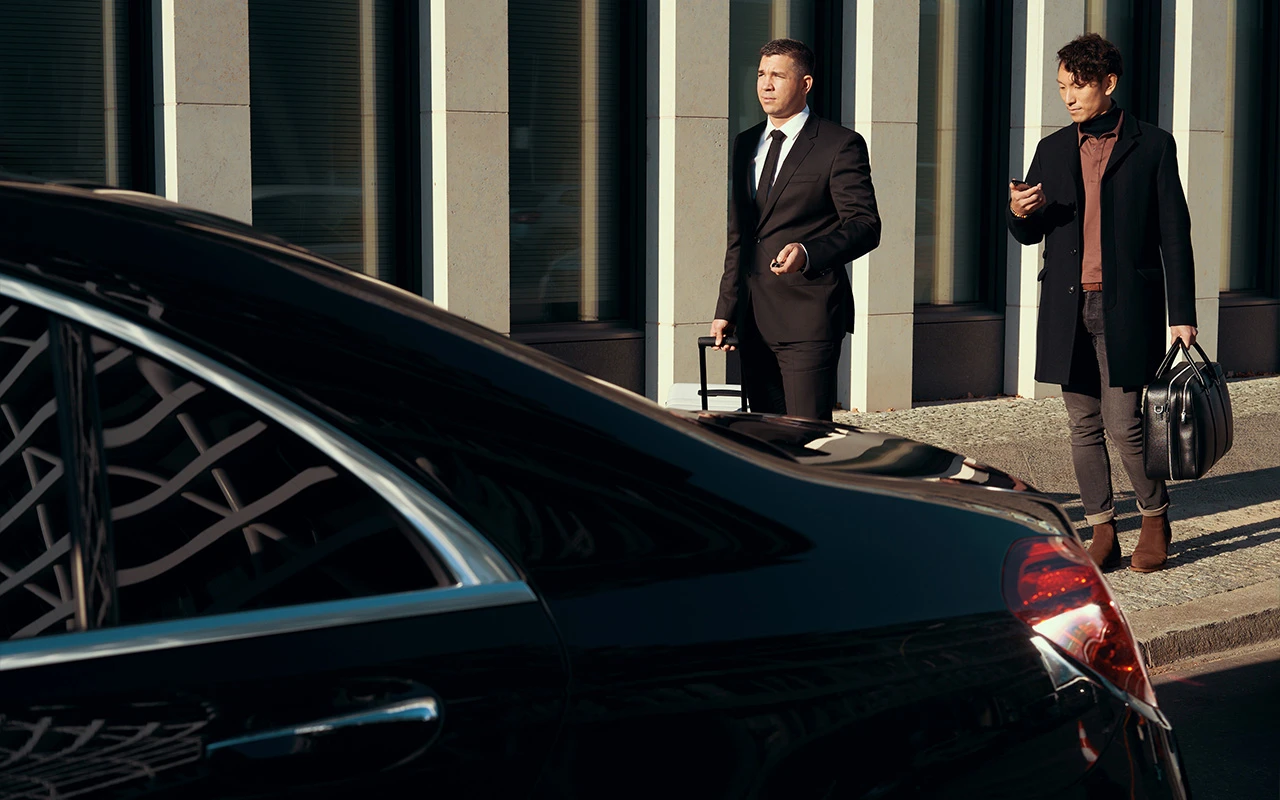 Chauffeur and family standing around a sleek, black vehicle.